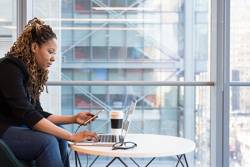 Modern work image of a woman sitting in a high-rise office with a phone and laptop, working through a planned migration of Microsoft Teams Phone.