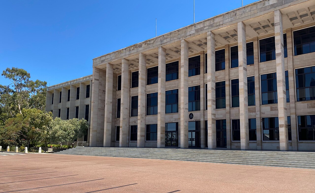 Exterior view of Parliament House in Perth Central Business District, Western Australia, featuring its modern stone colonnade and grand forecourt under a clear blue sky.