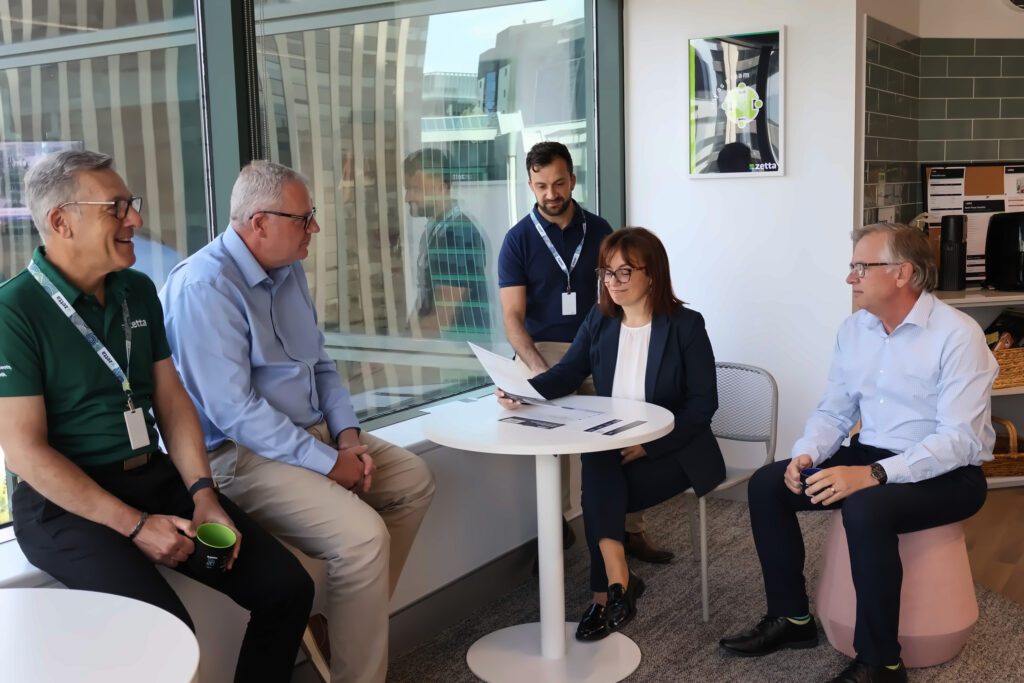 Zetta team members review a document at a round table by the window, Perth CBD towers outside.