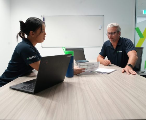 Two Zetta team members talking through a document at a meeting table, with a laptop open