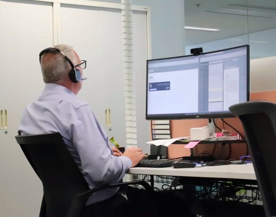 Zetta team member wearing a headset and working at a curved monitor in the Perth office