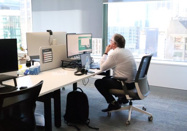 Zetta team member working at a hot desk beside floor-to-ceiling windows overlooking the Perth CBD