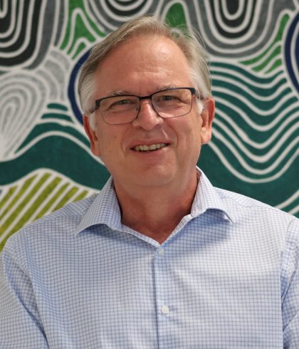 Simon Bendotti, Zetta Operational Services Manager, smiling in front of Aboriginal artwork in the Perth office