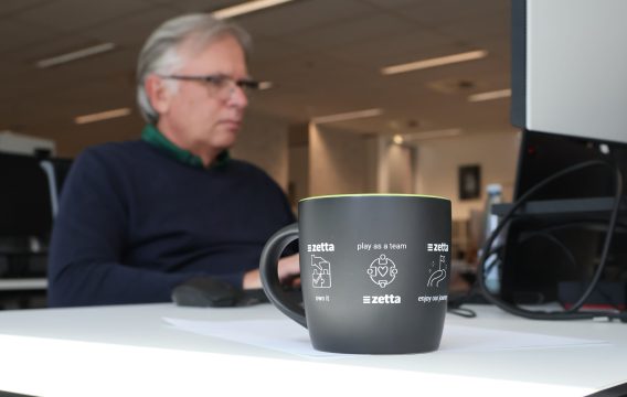 Zetta values mug on a desk, with a Zetta team member working behind