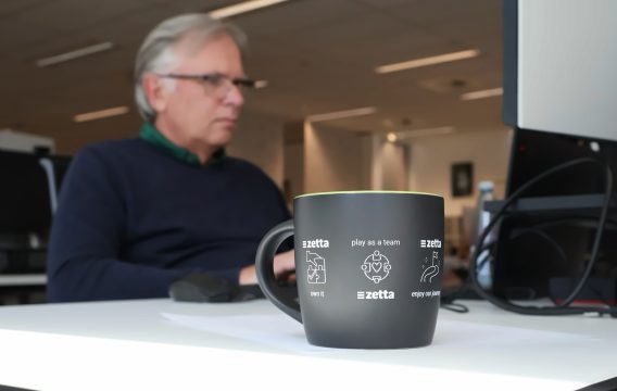 Zetta values mug on a desk, with a Zetta team member working behind